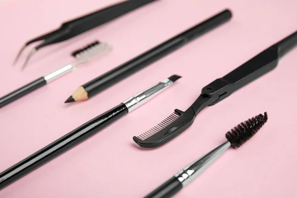 Set of professional eyebrow tools on pink background