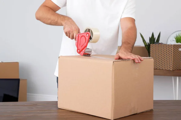 Young worker packing cardboard box in room, closeup. Moving service