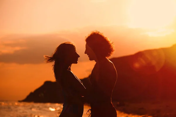 Młoda kobieta w bikini i jej chłopak na plaży o zachodzie słońca. Piękna para — Zdjęcie stockowe