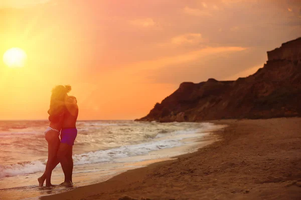 Young woman in bikini and her boyfriend on beach at sunset. Lovely couple — Stock Photo, Image