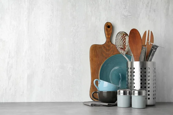 Different kitchen utensils on grey table against light background. Space for text — Stock Photo, Image