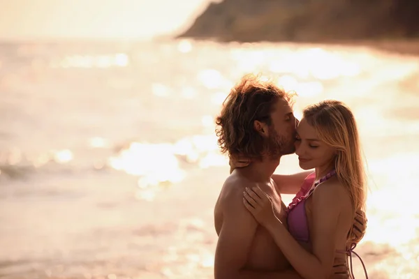 Mujer joven en bikini besando a su novio en la playa al atardecer. Hermosa pareja. — Foto de Stock