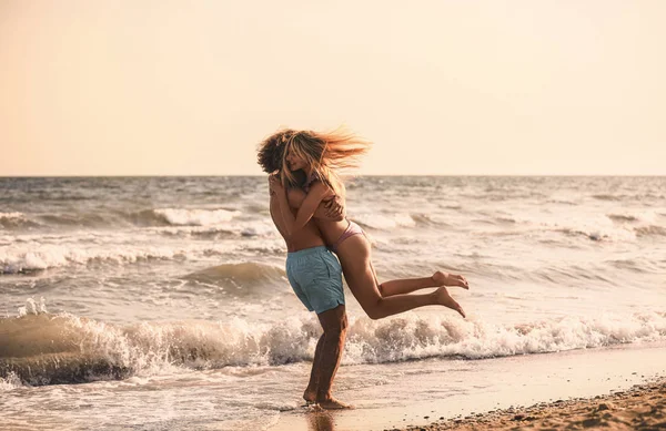 Mujer joven en bikini y su novio divirtiéndose en la playa al atardecer. Hermosa pareja. —  Fotos de Stock