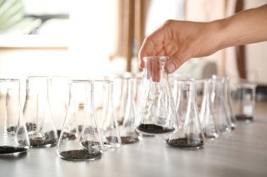 Masanın üzerinde toprak örneği olan şişe tutan kadın, yakın çekim. Laboratuvar analizi