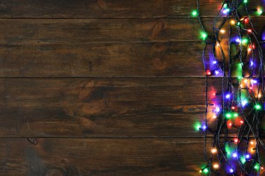 Kahverengi ahşap arka plan üzerinde Parlayan Noel ışıkları, üst görünümü. Metin için alan
