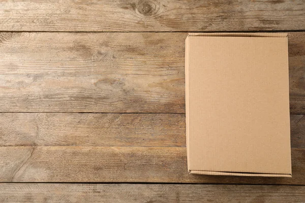 Closed cardboard box on wooden background, top view. Space for text — Stock Photo, Image