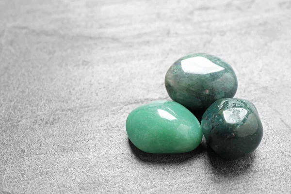 Beautiful green gemstones on grey table, space for text