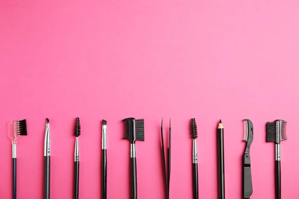 Set of professional eyebrow tools on pink background, flat lay. Space for text