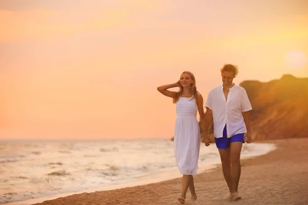 Pareja joven caminando en la playa al atardecer — Foto de Stock