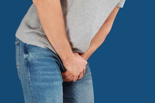 Man suffering from pain on blue background, closeup. Urology problems
