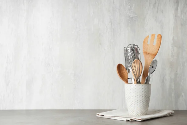 Holder with kitchen utensils on grey table against light background. Space for text — Stock Photo, Image