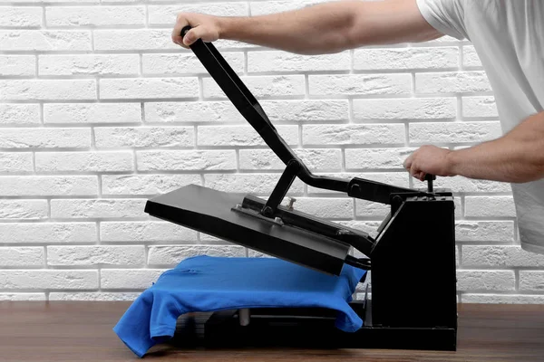 Man using heat press machine at table near white brick wall, closeup