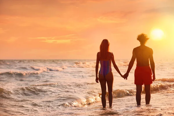 穿着比基尼的年轻女子和她的男朋友在日落时分在海滩上。可爱的夫妇 — 图库照片