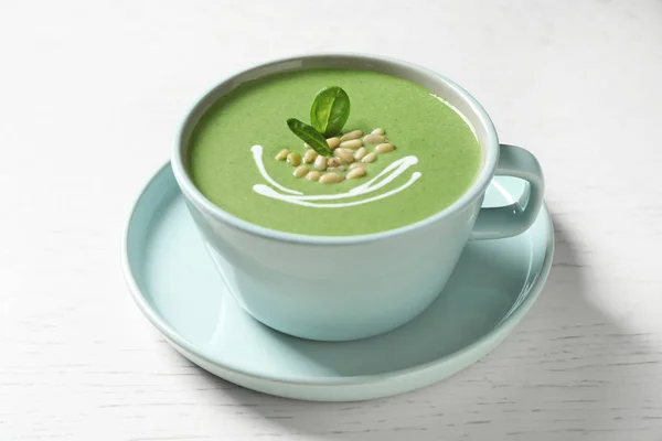 Cup of healthy green soup with fresh spinach on white wooden table