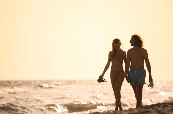 Mujer joven en bikini y su novio caminando en la playa al atardecer. Hermosa pareja. —  Fotos de Stock