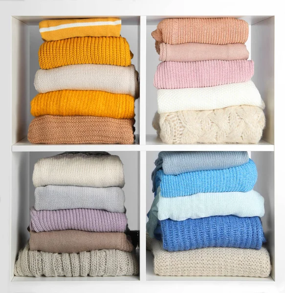 De nombreux vêtements d'hiver tricotés empilés sur des étagères sur fond blanc — Photo