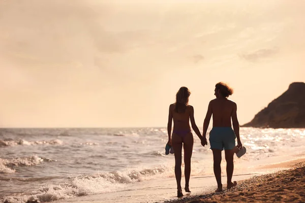 Mujer joven en bikini y su novio caminando en la playa al atardecer. Hermosa pareja. — Foto de Stock