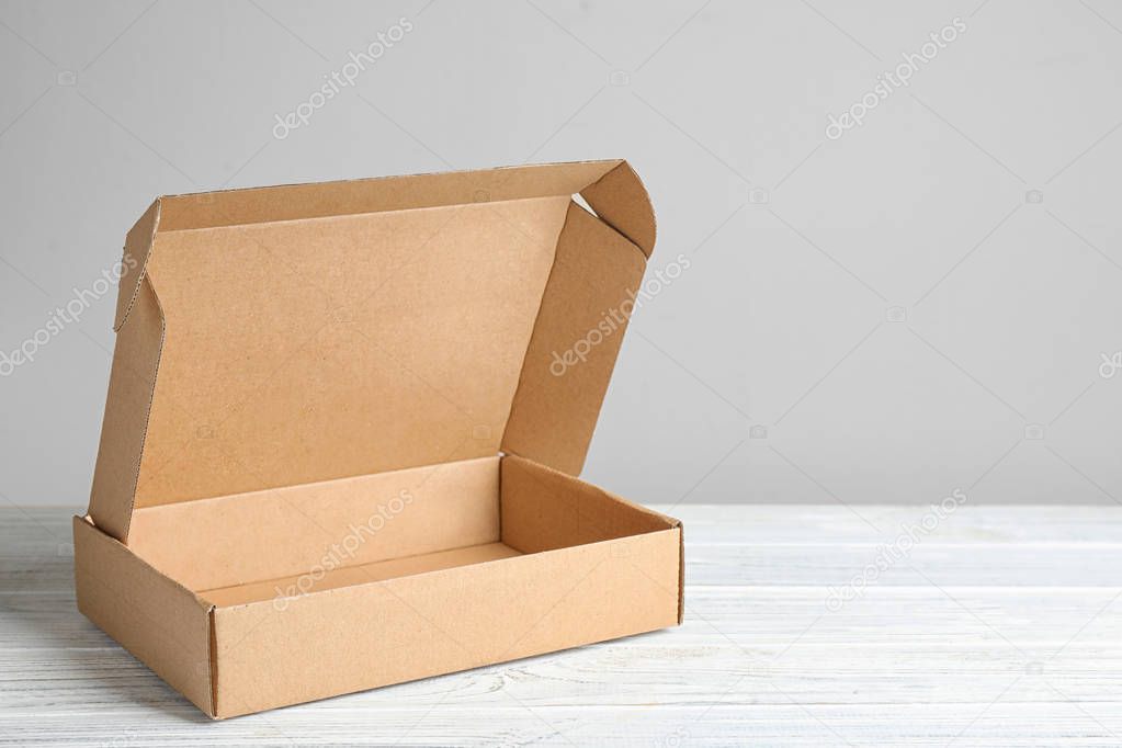 Open cardboard box on white wooden table against beige background, space for text