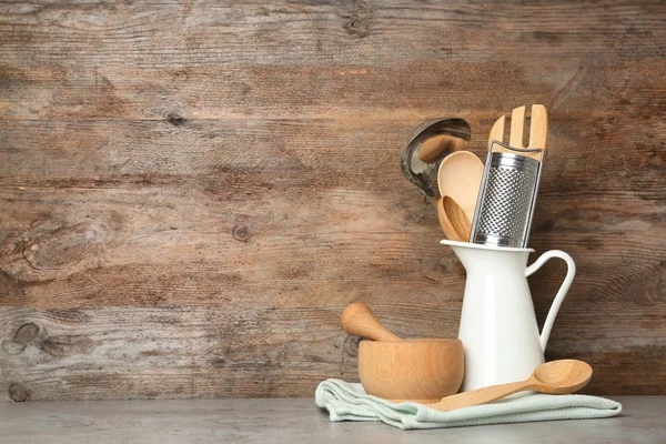 Different kitchen utensils on grey table against wooden background. Space for text — Stock Photo, Image