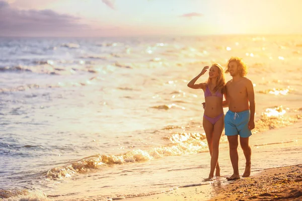 Młoda kobieta w bikini i jej chłopak na plaży o zachodzie słońca. Piękna para — Zdjęcie stockowe