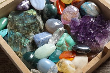 Box with different beautiful gemstones on table, closeup clipart