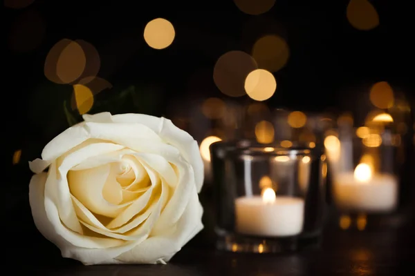 Witte roos en brandende kaarsen op tafel in duisternis. Begrafenis symbool — Stockfoto