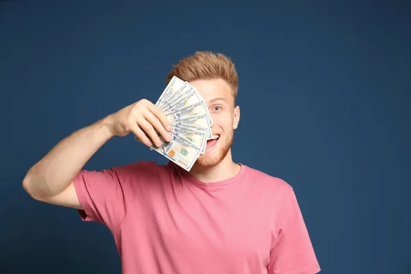 Portret szczęśliwego zwycięzcy loterii z fanem pieniędzy na niebieskim tle — Zdjęcie stockowe