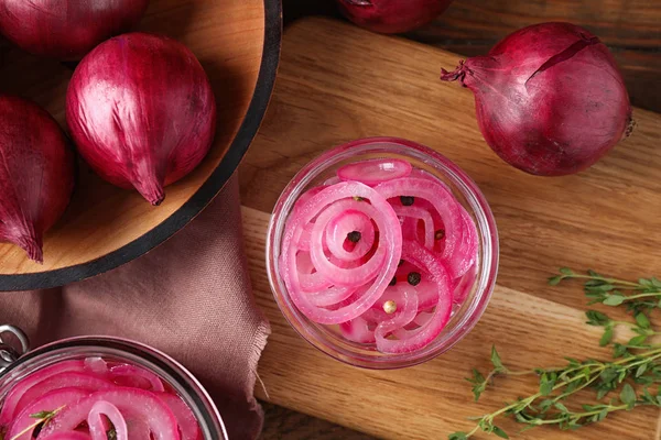 Composition with tasty pickled onions on wooden cutting board, flat lay