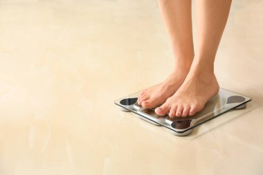 Woman standing on scales indoors, space for text. Overweight problem clipart