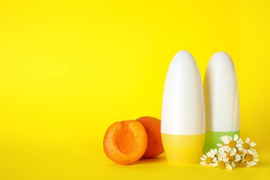 Sarı arka planda dişi roll-on deodorantlar, kayısı ve papatya çiçekleri, metin için alan