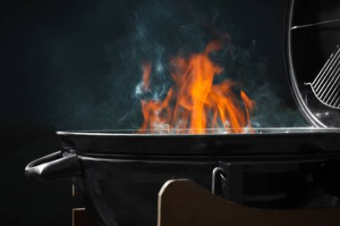 New modern barbecue grill with fire on dark background clipart