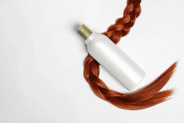 Botella en blanco de producto cosmético y cabello trenzado sobre fondo blanco, vista superior. Espacio para el diseño — Foto de Stock