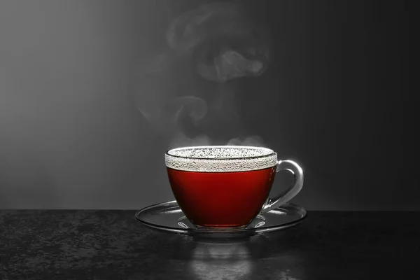Стеклянная чашка горячего чая на каменном столе на сером фоне, место для текста — стоковое фото