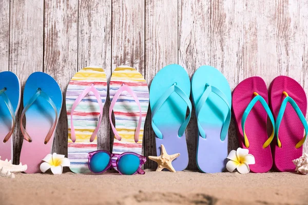 Different bright flip flops and sunglasses on sand near wooden wall, space for text. Summer beach accessories — Stock Photo, Image
