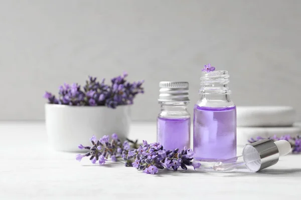Botellas de vidrio de aceite cosmético natural y flores de lavanda en mesa de madera blanca — Foto de Stock