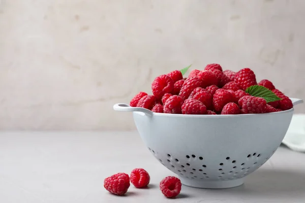 Colander com deliciosas framboesas maduras na mesa branca contra fundo claro, espaço para texto — Fotografia de Stock