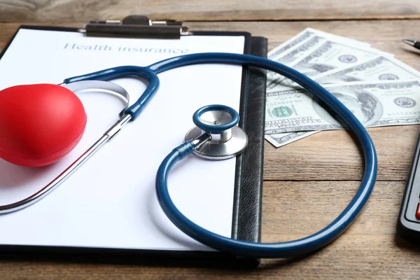 Форма медицинского страхования, красное сердце со стетоскопом и деньги на деревянной поверхности — стоковое фото