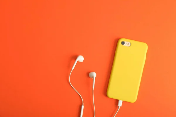 Modern phone with earphones on coral background, top view. Space for text