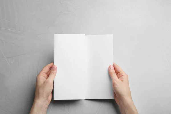 Joven mujer sosteniendo folleto en blanco en la mesa gris, vista superior. Prepárate para el diseño — Foto de Stock