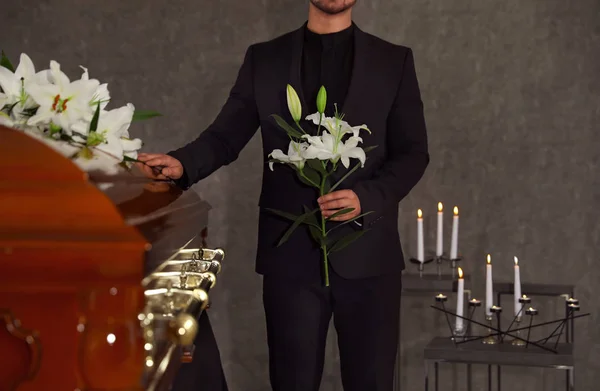 Young man with white lilies near casket in funeral home, closeup — Stock Photo, Image