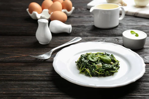 Placa con sabrosas espinacas cocidas sobre mesa de madera negra. Alimento saludable — Foto de Stock