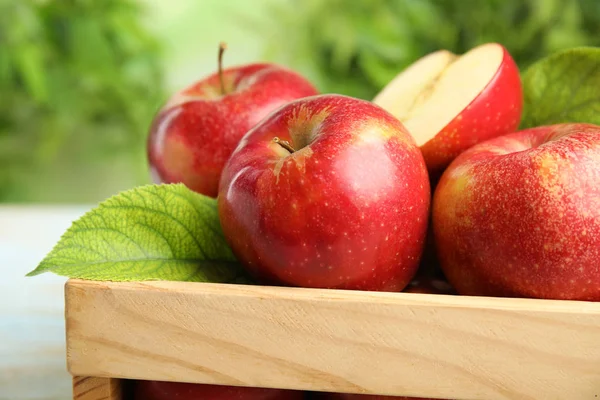 Caisse en bois avec des pommes rouges juteuses mûres sur fond flou, gros plan — Photo