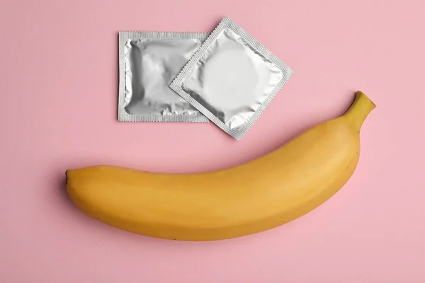 Preservativos com banana sobre fundo rosa, flat lay. Sexo seguro — Fotografia de Stock