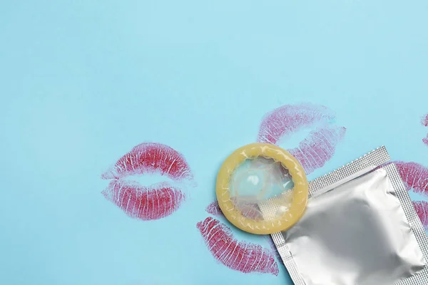 Condom with lipstick kiss marks and space for text on light blue background, flat lay. Safe sex