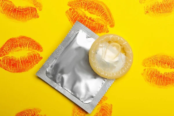 Condom with lipstick kiss marks on yellow background, flat lay. Safe sex