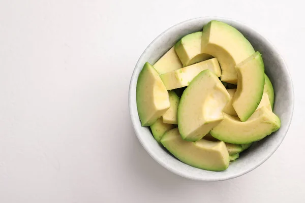 Bowl with cut avocados on white table, top view. Space for text