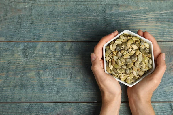 Jonge vrouw met Bowl van rauwe pompoenpitten op blauwe houten tafel, Top uitzicht. Ruimte voor tekst — Stockfoto