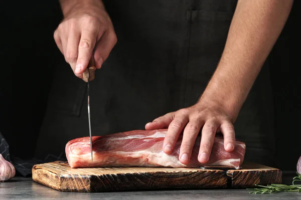 Hombre cortando carne fresca cruda en la mesa sobre fondo oscuro, primer plano — Foto de Stock