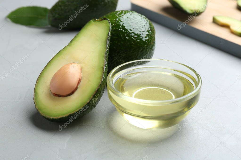 Bowl of natural oil and avocados on grey stone background