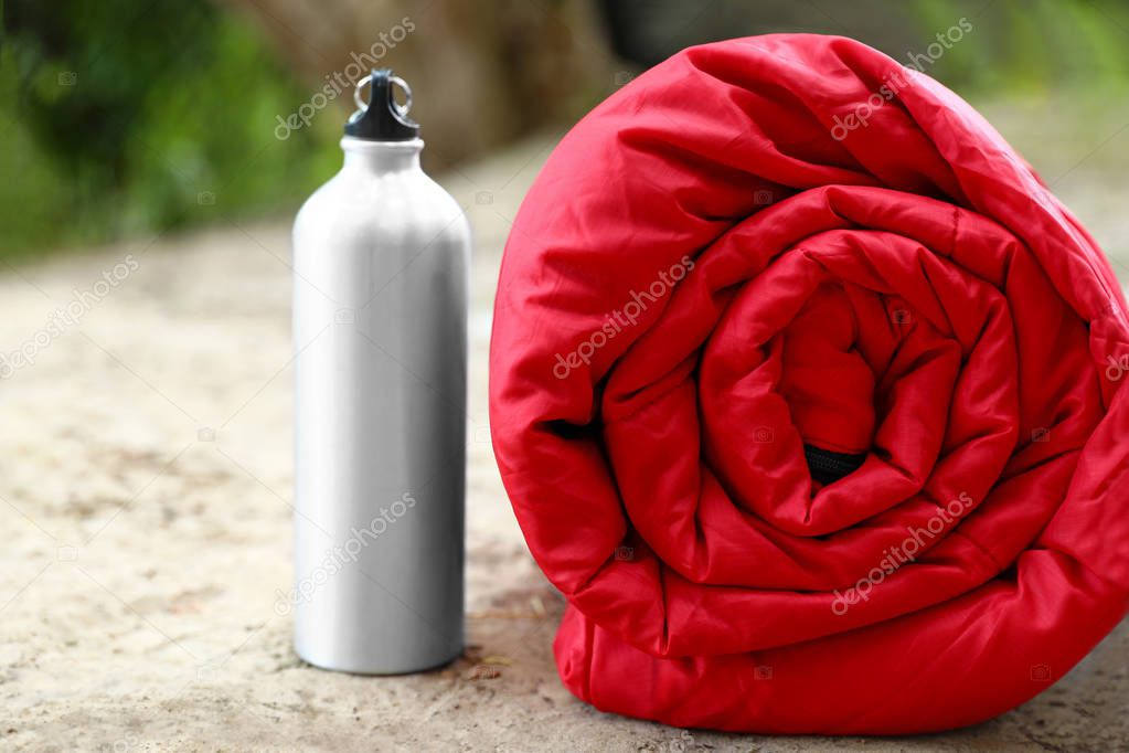 Rolled sleeping bag and bottle on sand